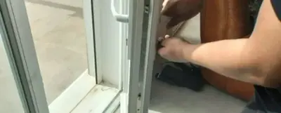 Mains réglant la quincaillerie d'une porte-fenêtre blanche